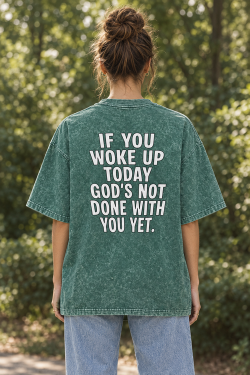 Model wearing the UNQLFD green mineral wash tee with Gods Not Done With You Yet back print