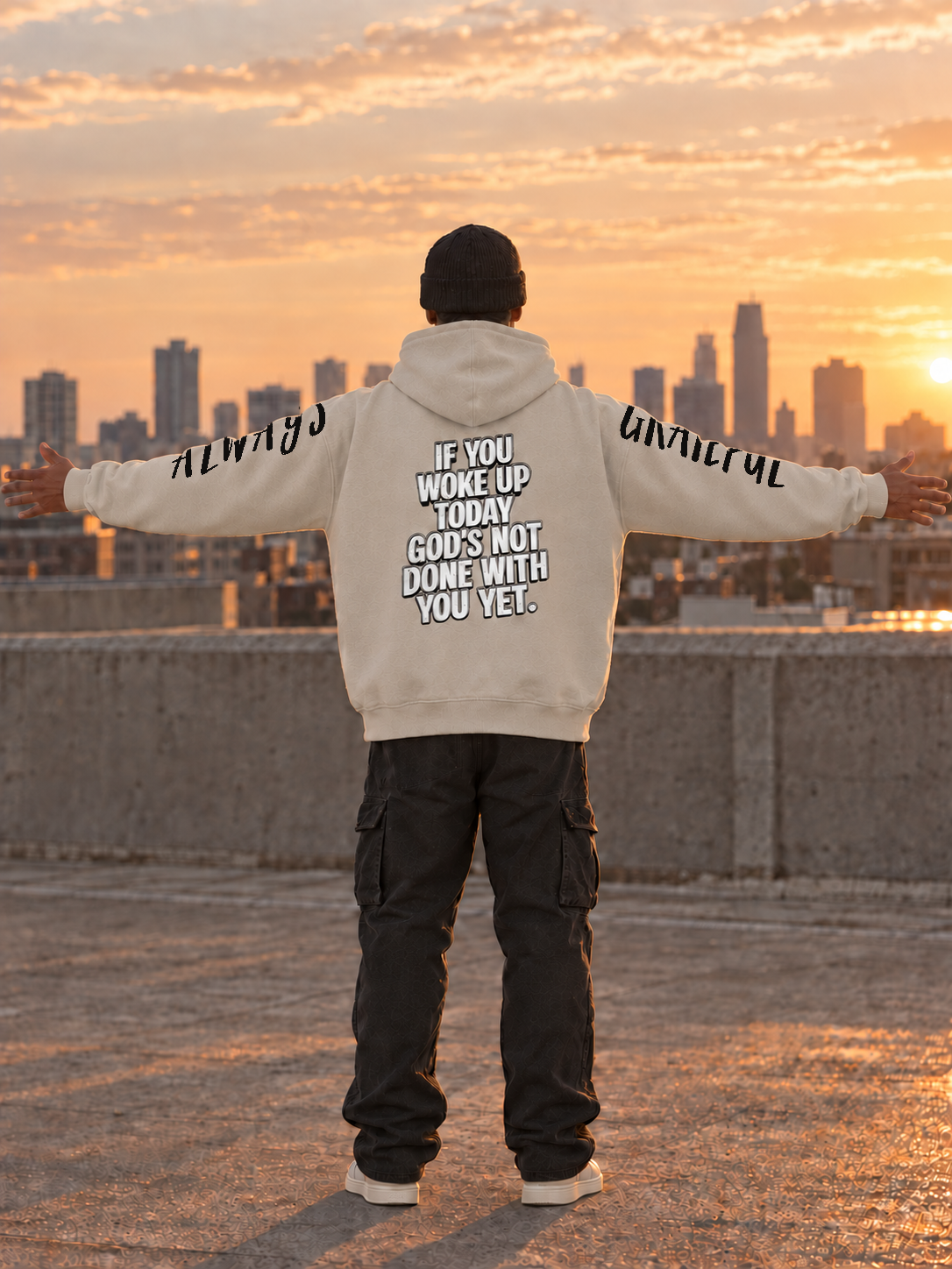 Generated back-view model photo of cream GODS NOT DONE hoodie with arms extended; supplied ALWAYS and GRATEFUL hand-lettered artwork is printed along the upper outer sleeves and partly wraps out of view. Original mockups show exact production artwork.